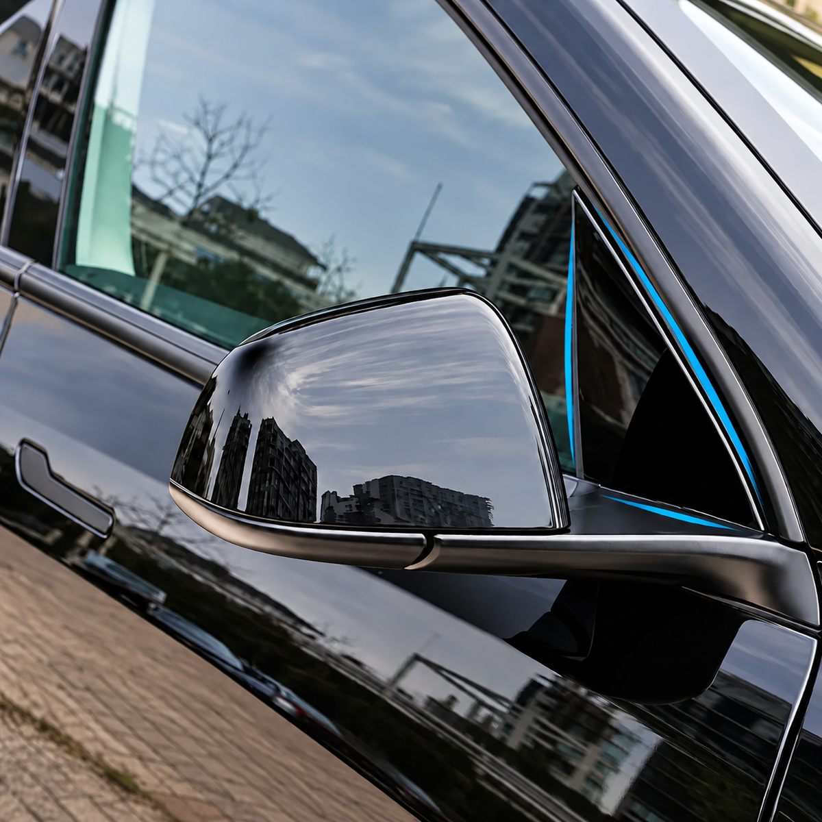 Close-up of a glossy black car side mirror and window trim with a thin blue accent line, reflecting an outdoor city scene.
