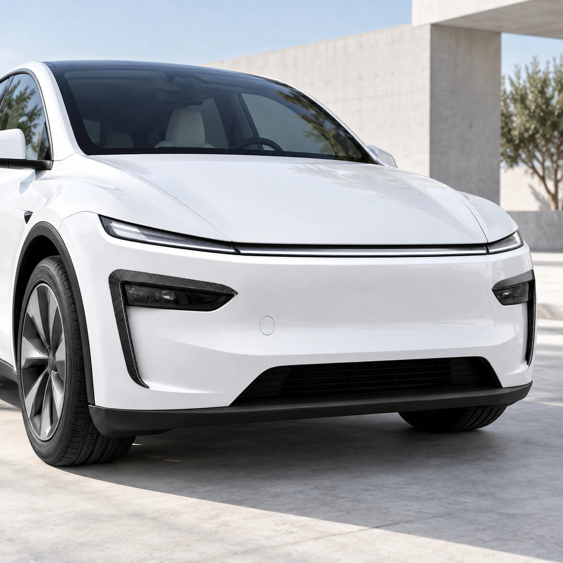 White Tesla Model Y Juniper with slim carbon-look front fog light trim in a modern architectural setting.
