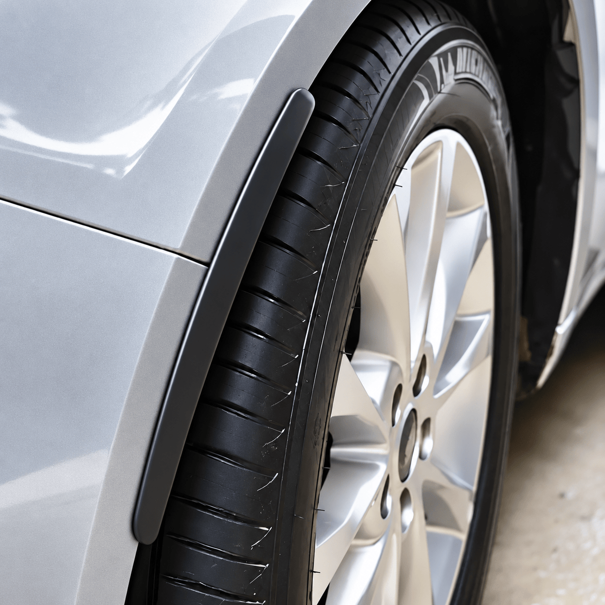 Black protector strip following the edge of a silver car's wheel arch